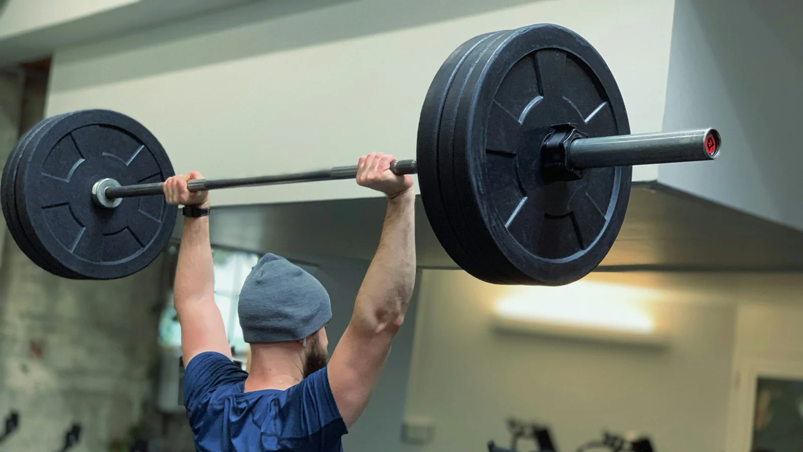 Person pressing a loaded barbell overhead in a gym