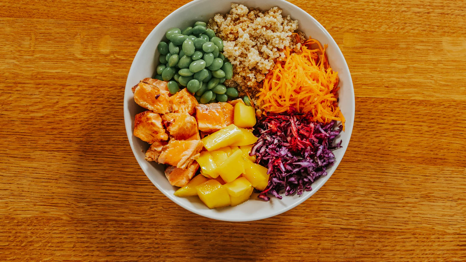 Colorful bowl with salmon, edamame, quinoa, carrot, mango, and red cabbage